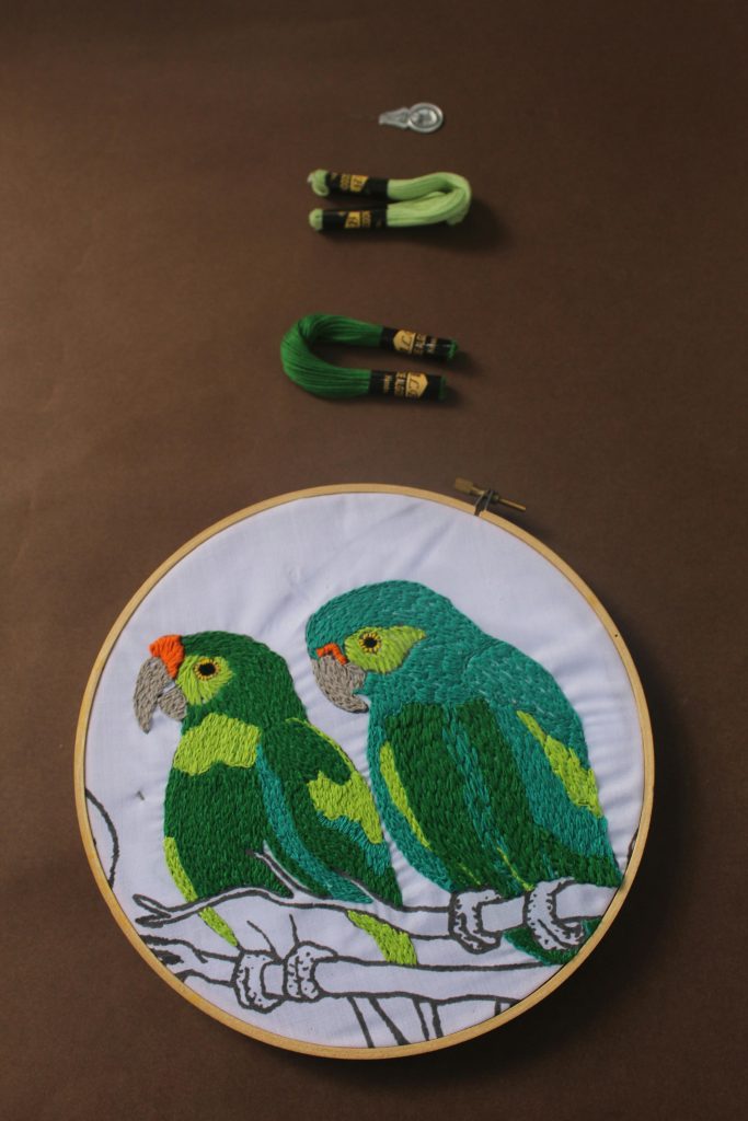 Colorful embroidered parrots on fabric in an embroidery hoop.