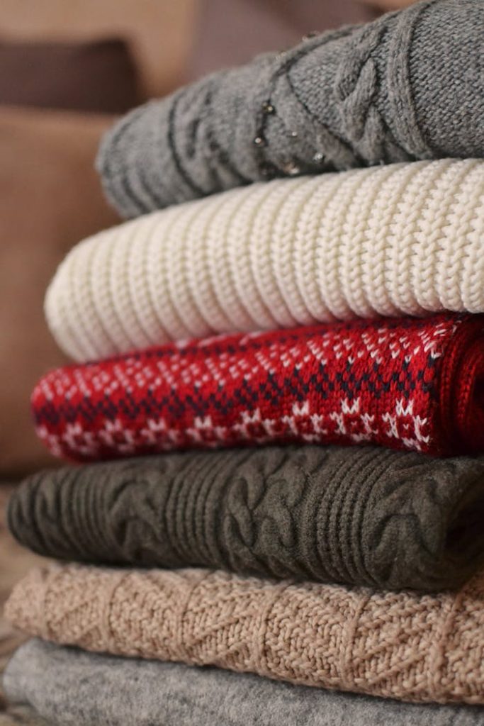 A pile of cozy folded sweaters in various colors and textures ready for winter wear.