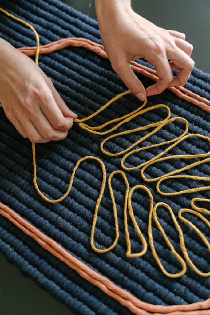 Close-up of hands arranging yarn into a pattern on textured fabric indoors.