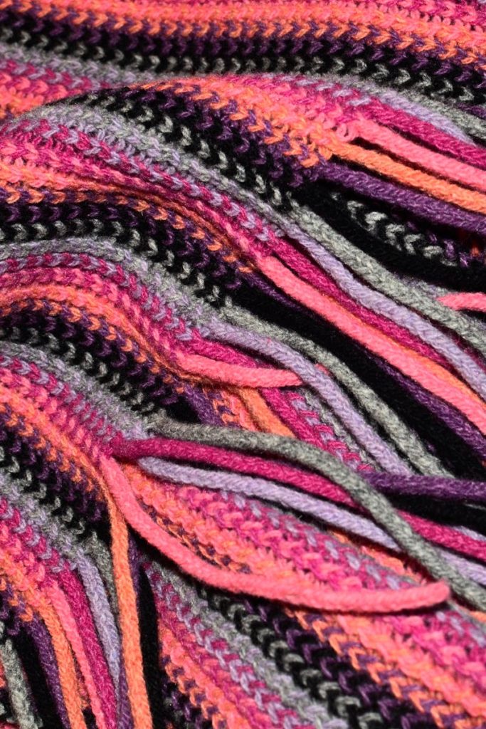 Full frame abstract background of colorful warm woolen scarf with long bright fringe